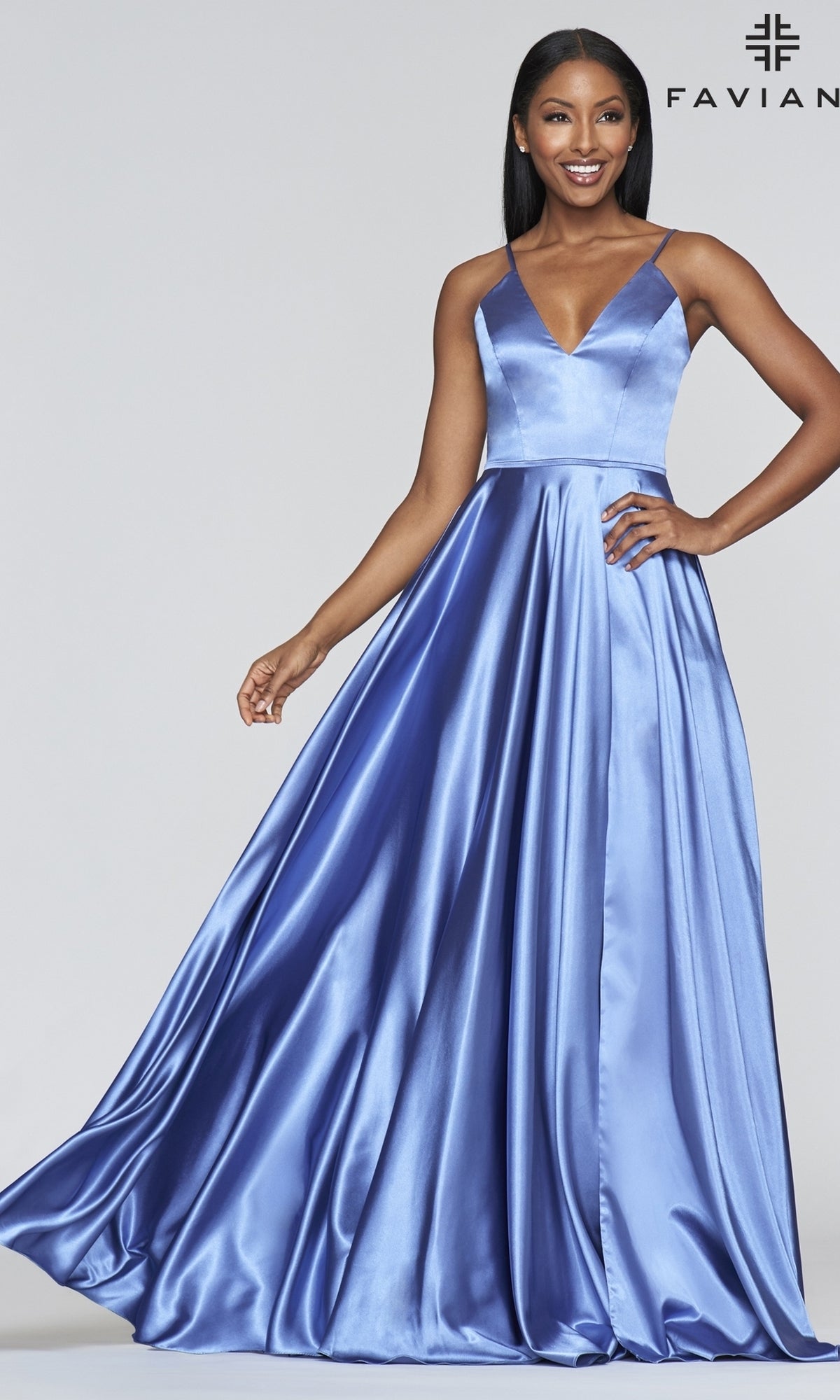 A woman stands smiling against a light background, wearing the Long Faviana Prom Dress, a sleeveless, floor-length blue satin gown with a V-neckline and stylish back cut-out.